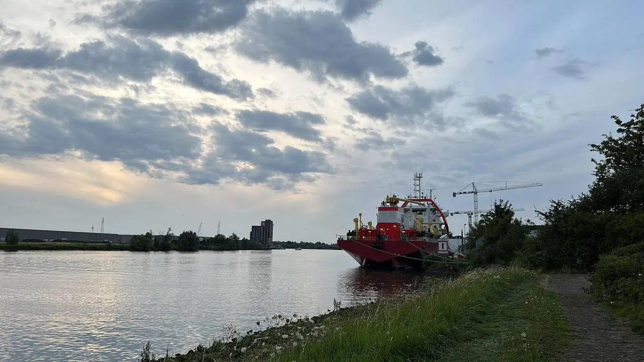 Rood werkschip vanaf de rivieroever bij avondlicht
